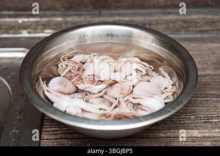 Primo piano di polpo fresco immerso in acqua all'interno di un recipiente in acciaio inossidabile, pronto per la preparazione dei frutti di mare o la cottura. Foto Stock