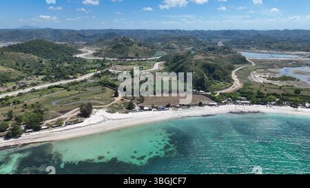 Le acque turchesi e le spiagge di sabbia bianca si snodano lungo la costa di Lombok. Colline ondulate e strade tortuose si estendono nell'entroterra sotto un luminoso cielo tropicale. Foto Stock