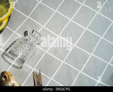 vodka limpida, fette di limone, testa di pesce secca su una tovaglia geometrica Foto Stock