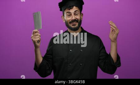 Chef ispanico in uniforme nera sorridente su un vivace sfondo viola che mostra entusiasmo culinario. Foto Stock