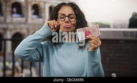 Donna di mezza età all'aperto presso il roman coliseum che tiene in mano banconote della corona islandese e fa un gesto di pianto, suggerendo delusione economica per tr Foto Stock