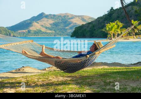 Uomo che si rilassa sull'amaca e gode della vista sul mare, sulle isole Yasawa e sulle Figi Foto Stock