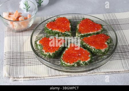 Cuori a forma di canape con caviale rosso su piatto rotondo su sfondo grigio, idea per la colazione di San Valentino Foto Stock