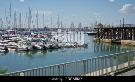 Le barche a vela attraccate in un soleggiato porticciolo di torrevieja con vista sul mare calmo, il cielo vivace e il molo in legno di alicante, in spagna, che mostrano un ambiente sereno Foto Stock