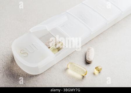 Organizzatore di pillole compatto per 7 giorni con fondo sagomato. Contenitore in plastica con diverse pillole su sfondo chiaro Foto Stock