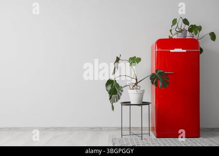 Frigorifero rosso e tavolo con piante d'casa vicino alla parete bianca in camera Foto Stock