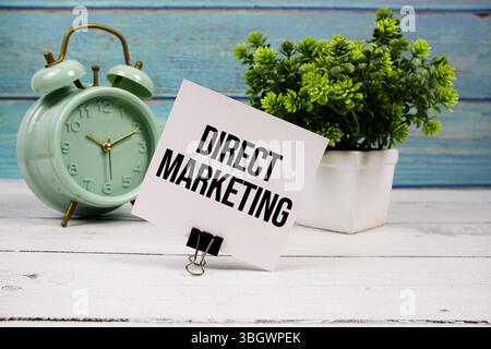 Testo di Direct Marketing scritto su carta con sveglia su sfondo in legno Foto Stock