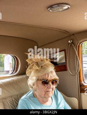 una donna più anziana che indossa un cappello seduto su un'auto d'epoca, cattura un momento nostalgico di guida classica e di eleganza senza tempo Foto Stock