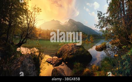 Maestose montagne nelle Alpi tedesche che si riflettono in un lago panoramico al tramonto. Paesaggio lungo la riva del lago con una spettacolare luce dorata Foto Stock