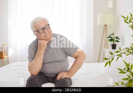 Uomo anziano che sogna sul letto in camera da letto durante la tranquilla mattinata a casa Foto Stock