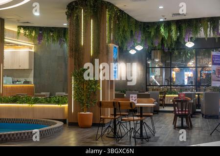 Bali, Indonesia - 17 dicembre 2024: Centro commerciale Trans Studio a Bali. Ristorante con una parete verde e una fontana blu. Ci sono diversi tavoli e sedie, e. Foto Stock