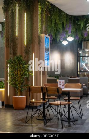 Bali, Indonesia - 17 dicembre 2024: Centro commerciale Trans Studio a Bali. Ristorante con una parete verde e una fontana blu. Ci sono diversi tavoli e sedie, e. Foto Stock