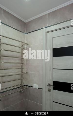 Grande e luminoso bagno in colori chiari con caldo pavimento piastrellato grigio, porta bianca contro la camera incompiuta. Foto Stock