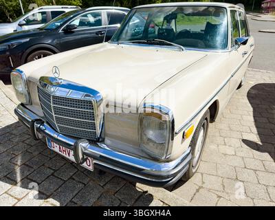 Auto d'epoca beige Mercedes-Benz W115 parcheggiata in un ambiente soleggiato all'aperto circondato da altri veicoli Foto Stock