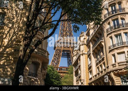 Una vista soleggiata della sezione centrale della Torre Eiffel incorniciata tra le facciate dei tradizionali edifici parigini Haussmanni, con luce solare Foto Stock