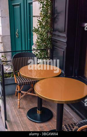 Un angolo intimo dell'area salotto esterna di un caffè parigino, caratterizzato da sedie da bistrot in tessuto nero e beige e tavoli rotondi con piani color ottone. Un lar Foto Stock