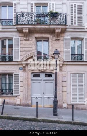 L'elegante entrata di un edificio parigino (numero 84) presenta una doppia porta grigia pallida, un balcone ornato in ferro battuto sopra e una classica l nera Foto Stock