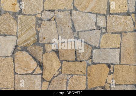 Immagine ad alta risoluzione di un muro in pietra testurizzata senza cuciture, caratterizzato da un motivo rustico in calde tonalità beige. Ideale come sfondo o trama per il design Foto Stock