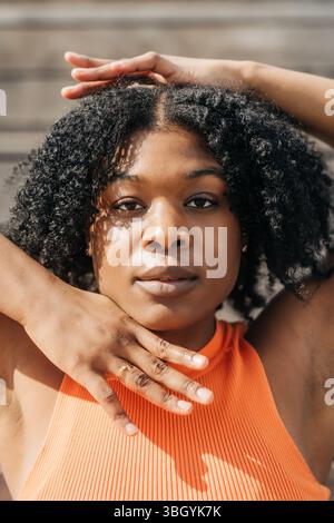 Primo piano di una donna con la parte superiore arancione con le mani che incorniciano il viso Foto Stock