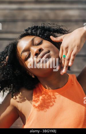Primo piano di una donna che sorride dolcemente con gli occhi chiusi alla luce del sole Foto Stock