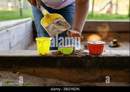 Bambini che giocano in una scatola di sabbia con secchi giocattolo e pala. Foto Stock