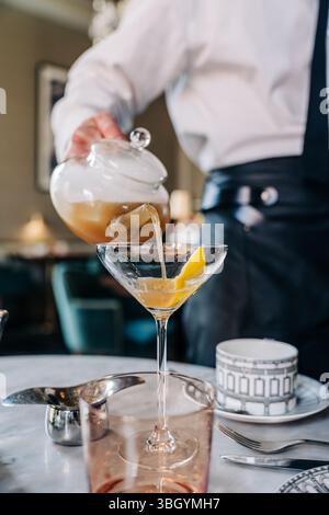 La bevanda viene versata dalla teiera nel bicchiere martini con limone Foto Stock