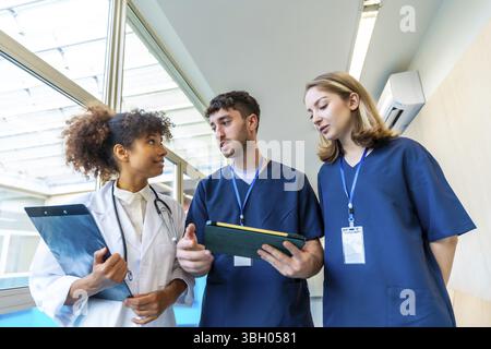 Medici e infermieri che esaminano cartelle cliniche e raggi X, collaborano alla cura dei pazienti in un corridoio ospedaliero Foto Stock
