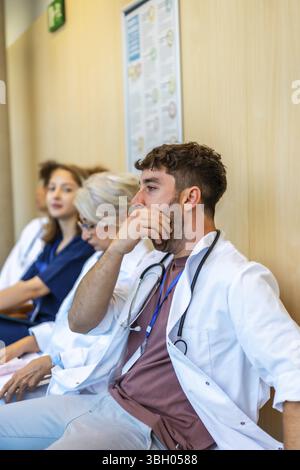 Gruppo di medici professionisti seduti in un corridoio dell'ospedale, sentendosi esausti dopo un lungo turno Foto Stock