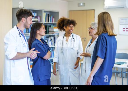 Diversi professionisti del settore medico collaborano, condividono competenze e strategie per un'assistenza ottimale al paziente all'interno di un ambiente ospedaliero Foto Stock