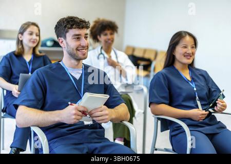 Gruppo di studenti di medicina sorridenti che partecipano a una conferenza, prendendo appunti e ascoltando il relatore nella sala conferenze universitaria Foto Stock