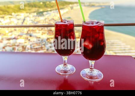 Primo piano di due bicchieri di Sangria che si affacciano sullo skyline di Nazare su sfondo sfocato. Concetto di festa, vacanza e aperitivo Foto Stock