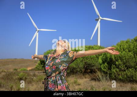 Una donna bionda appassionata di tecnologia ecologica gratuita delle turbine eoliche. Concetto di energia alternativa. Sagres, Algarve in Portogallo Foto Stock