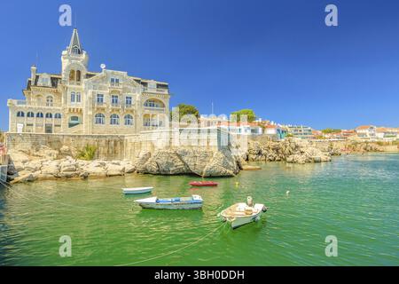 Paesaggio panoramico del Palazzo Seixas abbandonato e barche sul lungomare di Cascais, la costa di Lisbona in Portogallo. Praia da Rainha in lontananza. Turquoi Foto Stock