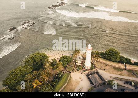 Vista aerea dall'alto verso il basso dello Sri Lanka, mentre fai una nuotata nell'oceano vicino all'iconico faro bianco al forte di Galle. La scena mescola l'architettura storica Foto Stock