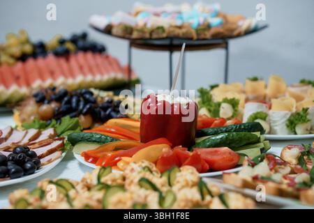 La colorata disposizione di cibo per feste è caratterizzata da peperoni ripieni di formaggio spalmabile, uva, formaggi e mini panini, presentati su un elegante bianco Foto Stock