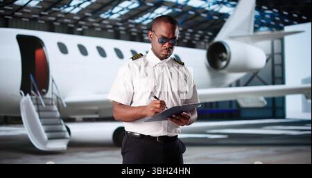 Sorridente pilota di linea afroamericano in uniforme controlla la manutenzione degli aeromobili Foto Stock
