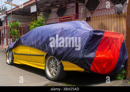 L'auto gialla è coperta da una copertura blu e rossa. L'auto è parcheggiata sul lato della strada Foto Stock