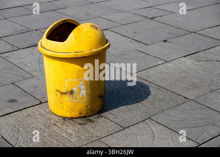 Il cestino giallo si trova su un pavimento in piastrelle grigie. Il cestino è vuoto." Concetto di responsabilità e pulizia Foto Stock