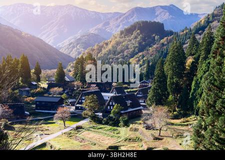 Soft morning light over Ainokura village in Toyama, Japan with gassho-style houses, forested hills and mountain backdrop during autumn season Foto Stock