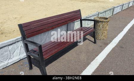 Panche di legno e cestini della spazzatura fiancheggiano il lato della strada in un'area ricreativa del parco. Estate Foto Stock