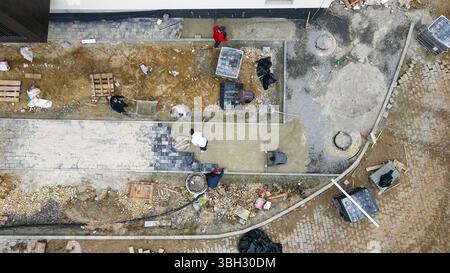 Vista aerea dei lavoratori che pavimentano un cantiere edile. Vista dall'alto verso il basso dei lavoratori che pavimentano e costruiscono un sito, con attrezzi, materiali e lavori di terra Foto Stock