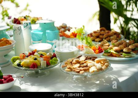 Il tavolo a buffet all'aperto offre diversi piatti, tra cui frutta fresca, mini hamburger, pasticcini e bevande colorate. Disposti su piatti, perfetti per eventi Foto Stock