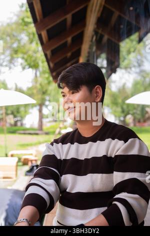 Giovane e carino uomo gay seduto all'aperto nel bar ristorante durante il giorno Foto Stock