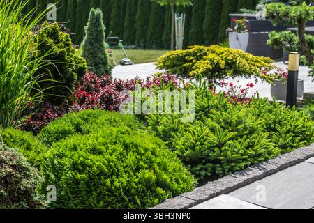 Un giardino splendidamente organizzato presenta una varietà di piante, tra cui lussureggianti arbusti verdi e fiori colorati, sotto cieli azzurri, che mettono in risalto na Foto Stock