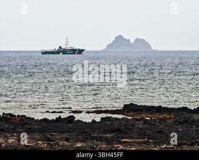 Una motovedetta Guardia Civil opera lungo la costa settentrionale di Lanzarote, supervisionando le acque con l'isola di Alegranza in lontananza. Foto Stock