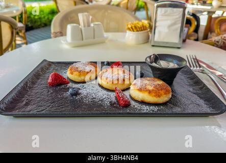 Sciroppi tradizionali, o frittelle di formaggio, serviti con frutti di bosco freschi e panna acida per la colazione sulla terrazza del ristorante. Deliziosi sciroppi per Foto Stock