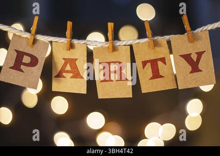 La parola PARTY è stampata su biglietti ritagliati di clothespin davanti a luci incandescenti sfocate Foto Stock