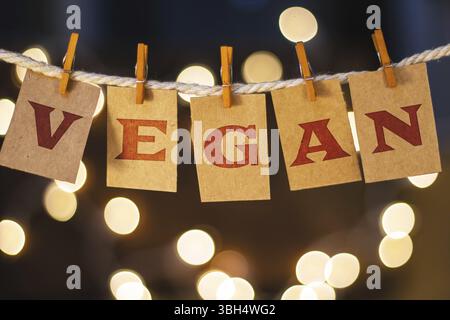 La parola VEGAN è stampata su carte clothespin tagliate davanti a luci incandescenti sfocate Foto Stock