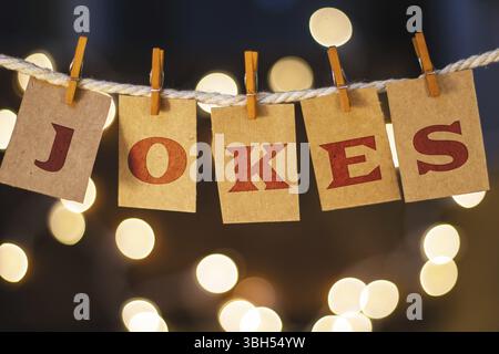 La parola BARZELLETTE è stampata sulle carte clothespin tagliate davanti a luci incandescenti sfocate Foto Stock