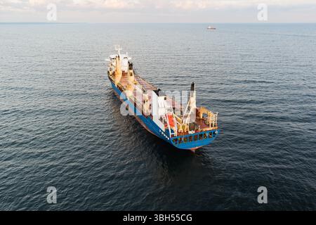 Vista aerea di una grande nave da carico generale blu e rosso che naviga sulle acque calme del Mar Baltico vicino alla costa dell'Estonia. Foto Stock